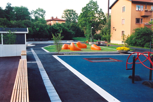 Forskellige farver og materialer markerer legepladsens områder. De orange glasfiberfigurer lyser om aftenen